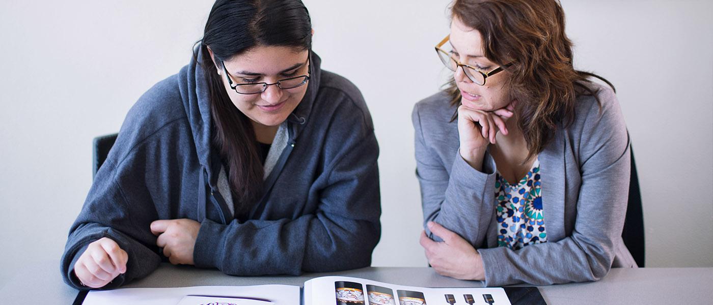 Professor going over samples of design work in a book with a student