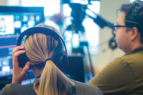 Over the shoulder view of communications students sitting in the studio working on a broadcast