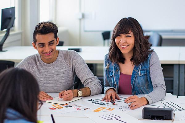 Smiling design students sitting at a table discussing their work